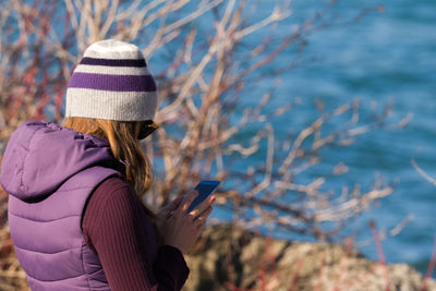 Side view of woman using mobile phone while standing against lake