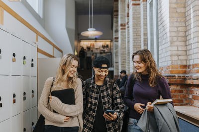 Smiling man sharing smart phone to female friends while walking in corridor