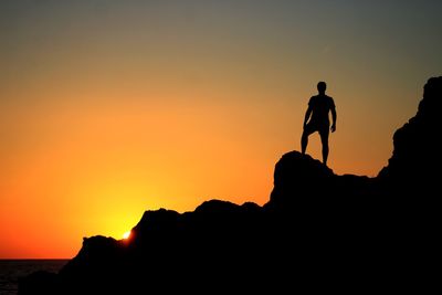 Silhouette people on cliff against orange sky