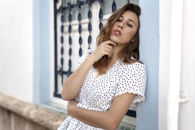 Beautiful young woman looking away while standing against wall