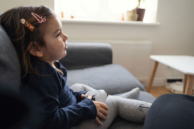 Side view of girl sitting on sofa at home