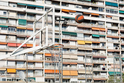 Ball flying toward a basket with a residential building in the background,  urban outdoor sports. 