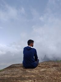 Rear view of man sitting on rock