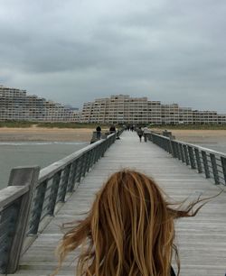 Rear view of woman on pier against cloudy sky