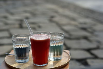 Cappuccino, macchiato, raspberry lemonade and two water glasses on a wooden tray, in a public park