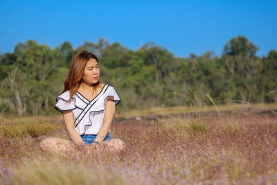 Young woman with flowers on field against clear blue sky