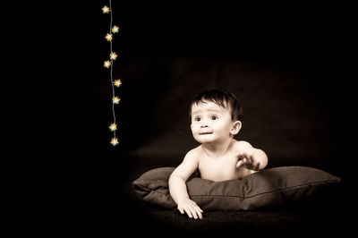 Cute boy on pillow looking at illuminated string lights against black background