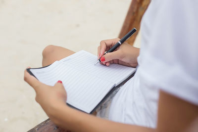 Midsection of woman writing in book while sitting on bench