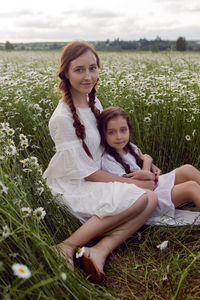 Mother with daughter in a white dress and hat stand in a daisy field in summer