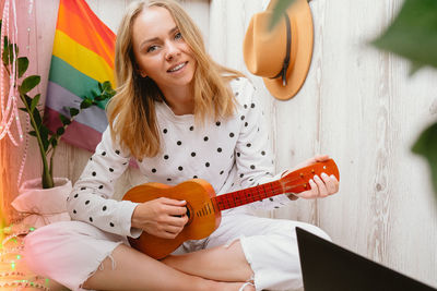 Young millennial hippie woman sitting on balcony play guitar. music lesson and singer sitting. lgbtq 