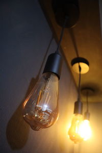 Low angle view of illuminated light bulb hanging from ceiling