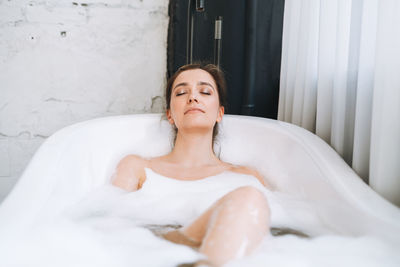 Young happy woman taking bath with foam at home, treat yourself