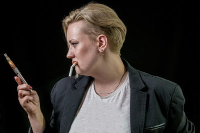 Sad young woman with electronic cigarette against black background
