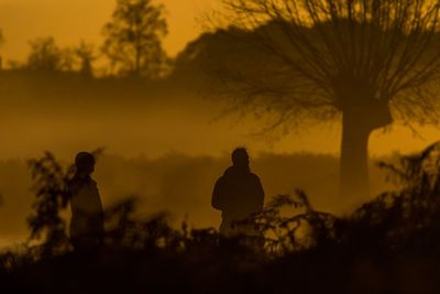 Silhouette men on field during foggy weather at sunset