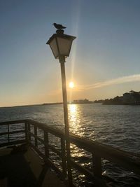 Street light by sea against sky during sunset