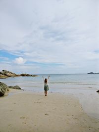 Rear view of woman standing on beach against sky