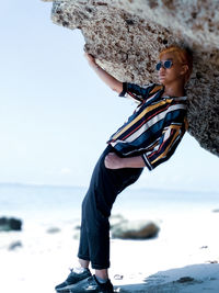 Midsection of woman on rock at beach against sky
