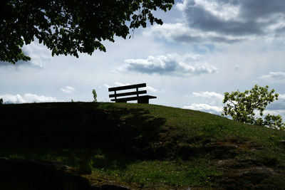 Bench on field by trees against sky