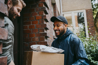 Smiling courier delivery person talking with man while delivering packages at doorstep