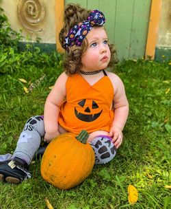 Full length of cute girl sitting by pumpkin on grass