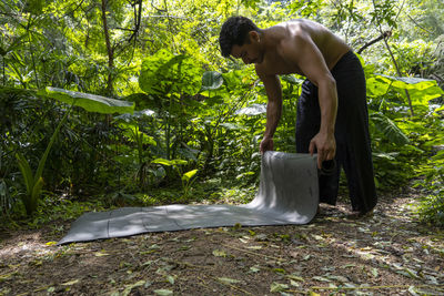 Young latin man arranging his yoga mat, inside a forest on a plain, direct contact with nature