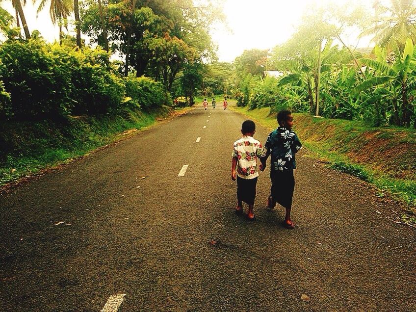 REAR VIEW OF FATHER WALKING ON ROAD AGAINST TREES