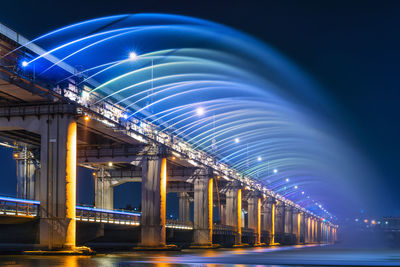 Illuminated bridge against blue sky at night