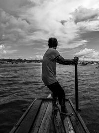 Rear view of man guiding the boat on the sea against sky