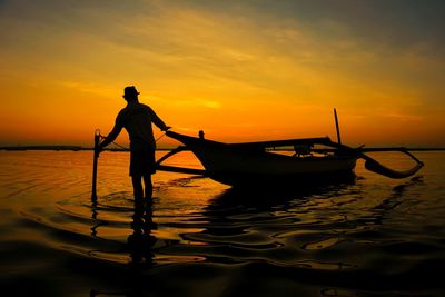 Silhouette man standing on shore against orange sky