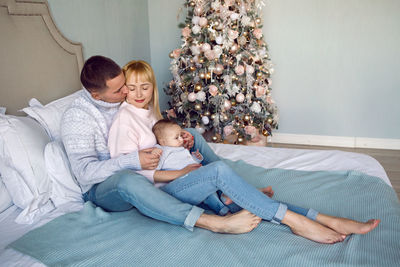 Family with son sitting on the bed next to the christmas tree at home