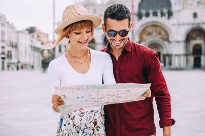 Happy couple reading map while standing in city