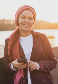 Portrait of young woman standing against lake during sunset