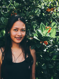 Portrait of smiling young woman standing against tree