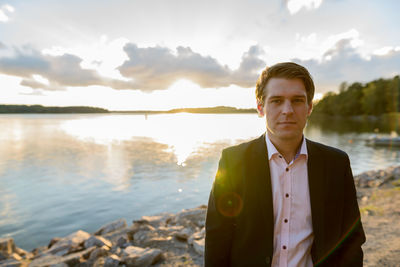 Portrait of young man standing by lake against sky