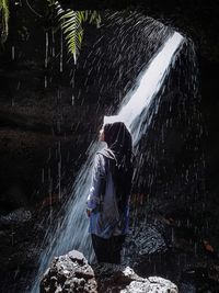 Rear view of person standing by waterfall in forest