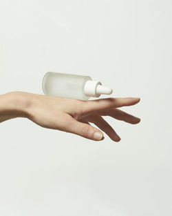 Hand of crop anonymous person with glass bottle of hyaluronic acid for skin care treatment on white background in light room person