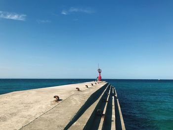 Concrete pier by sea against blue sky