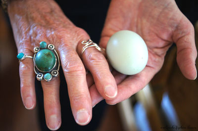 Cropped image of wrinkled hand wearing green ring holding white stone