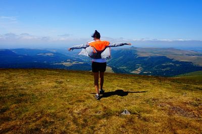 Rear view of woman with arms outstretched on mountain against blue sky