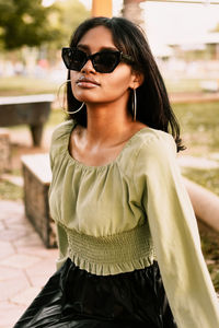Portrait of young brown skin woman wearing sunglasses and green blouse and black skirt