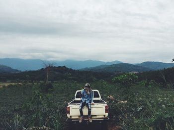 Full length of person sitting on pick-up truck at field