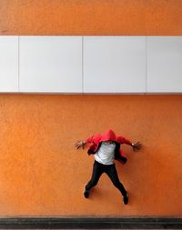 Young man wearing hood jumping against wall