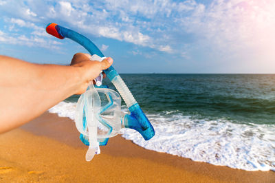 Rear view of woman holding water at beach against sky