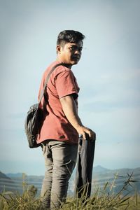 Young man looking away while standing on field against sky