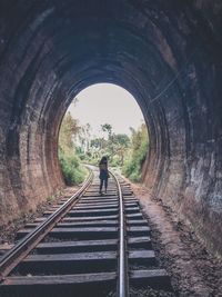 Rear view of woman walking on railroad track in tunnel