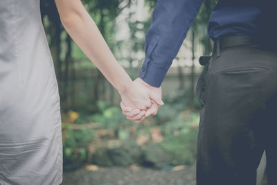 Midsection of couple holding hands while standing at park