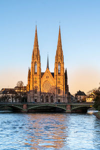 View of building by river against clear blue sky