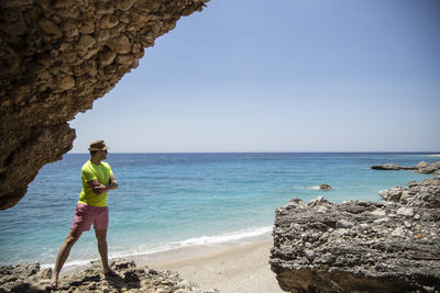 Man standing on rock by sea against sky