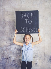 Portrait of smiling girl holding writing slate with text against wall