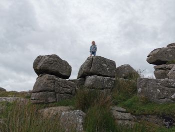 Low angle view of girl standing on rock against sky. dartmoor 